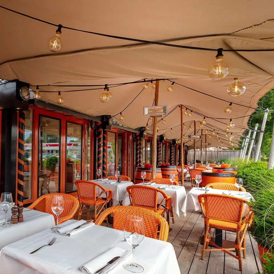 Terras met oranje stoelen onder een luifel met lichtjes